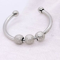 Bague anti-stress argentée posée sur un fond clair, mettant en évidence ses perles texturées.