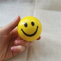 Balle anti-stress Smiley jaune avec un large sourire, tenue entre les doigts