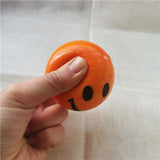 Balle anti-stress Smiley orange pressée entre le pouce et l’index, montrant sa déformation
