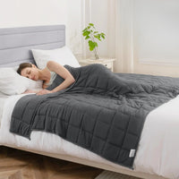 Couverture lestée 4 kg gris foncé posée sur un lit, illustrant un sommeil apaisé avec le modèle enfant.