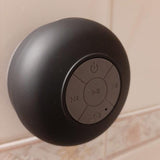 Enceinte portable waterproof noire fixée au mur de la salle de bain grâce à sa ventouse