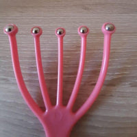 Gros plan sur la griffe masseuse de tête rose munie de cinq billes métalliques pour la détente du cuir chevelu