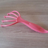 Griffe masseuse de tête rose vue de côté, avec poignée ergonomique et branches flexibles pour un massage relaxant