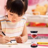 Une fillette concentrée sur son exercice, accompagnée d’un sablier de 30 minutes pour mieux organiser son temps d’apprentissage.