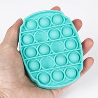 Press-in bubble turquoise tenu dans une main, montrant sa taille et ses bulles en silicone