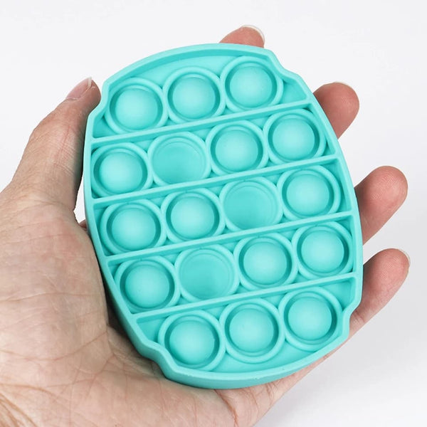 Press-in bubble turquoise tenu dans une main, montrant sa taille et ses bulles en silicone