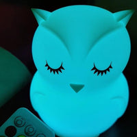 Veilleuse hibou à LED éclairée en bleu/vert, avec sa télécommande en arrière-plan 